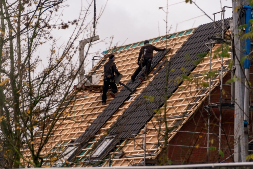 Higher Caliber Carpentry and Roofing Ltd workers shingling a steep roof.